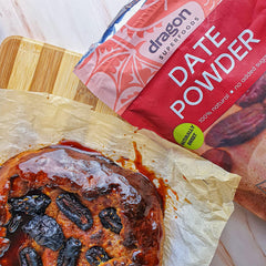 Bag of Dragon Superfoods date powder next to a dessert with dates on a wooden board.