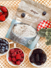 Bag of Dragon Superfoods Maca Powder with bowls of berries on a woven surface