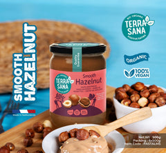 Terra Sana Smooth Hazelnut spread jar with hazelnuts and a wooden spoon on a blue background