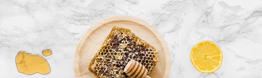 Raw honeycomb on a wooden plate with a honey dipper, a drizzle of liquid honey, and a fresh lemon slice.