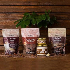 Dragon Organic Cacao Nibs, Cacao Powder, and Cacao Beans packages with a small container of Cacao Butter on a wooden surface.