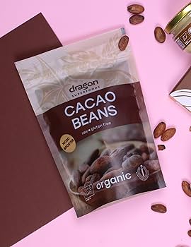 Bag of Dragon Organic Cacao Beans on a pink and brown background with scattered cacao beans.