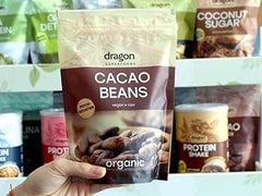 Hand holding a package of organic cacao beans with various health products in the background.
